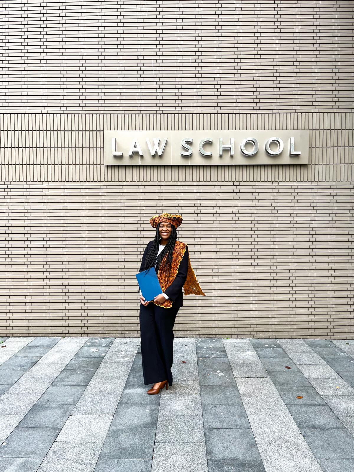 Winny voor een muur met het woord Law School en haar diploma in haar handen