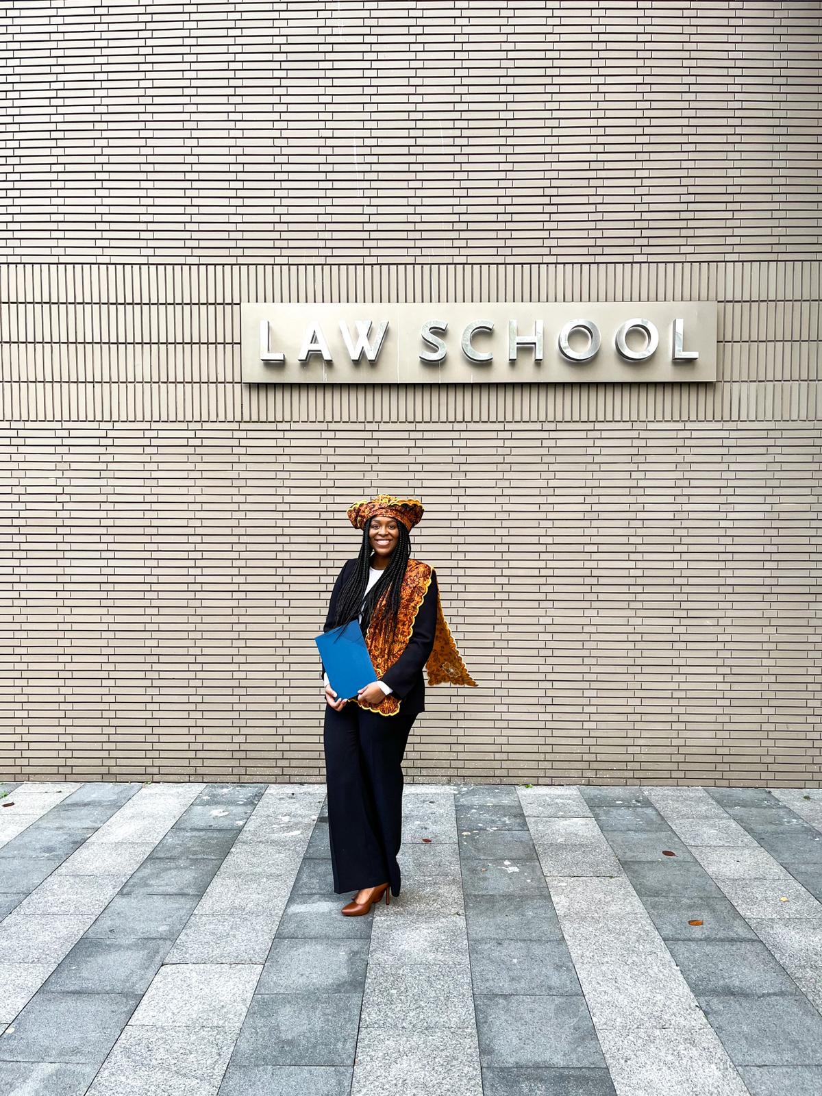 Winny voor een muur met het woord Law School en haar diploma in haar handen